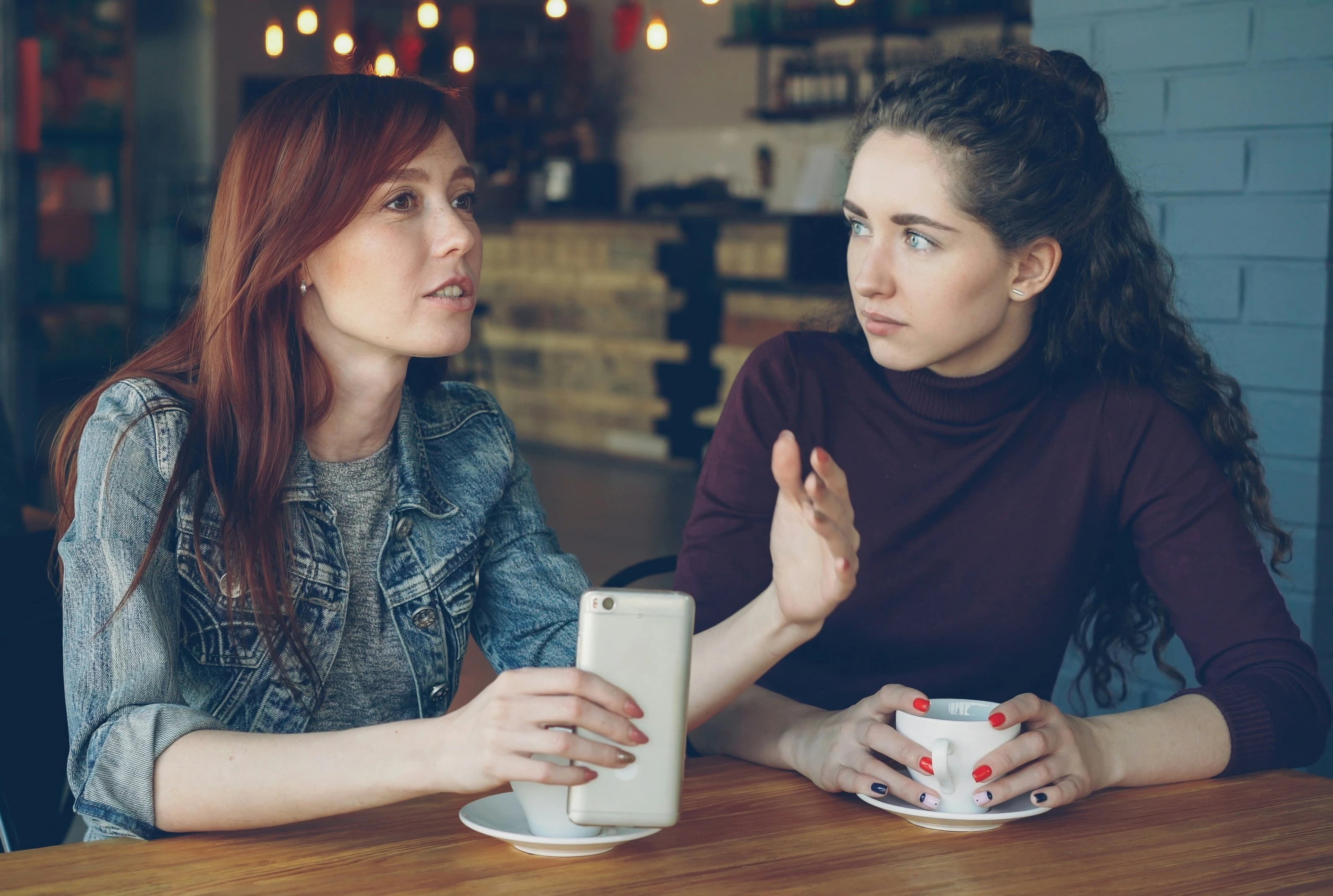 Two old friends reconnecting over coffee, smiling as one listens intently to the other. Familiar, comfortable, unhurried atmosphere.